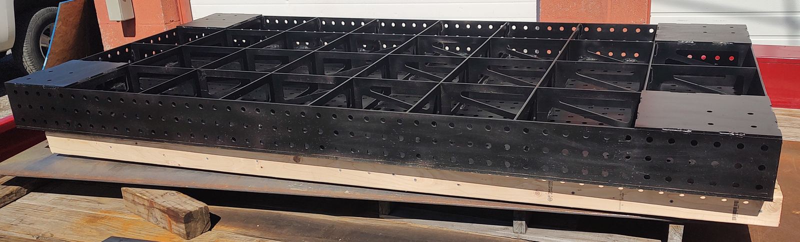 Black painted welding table underframe secured to a pallet on a trailer