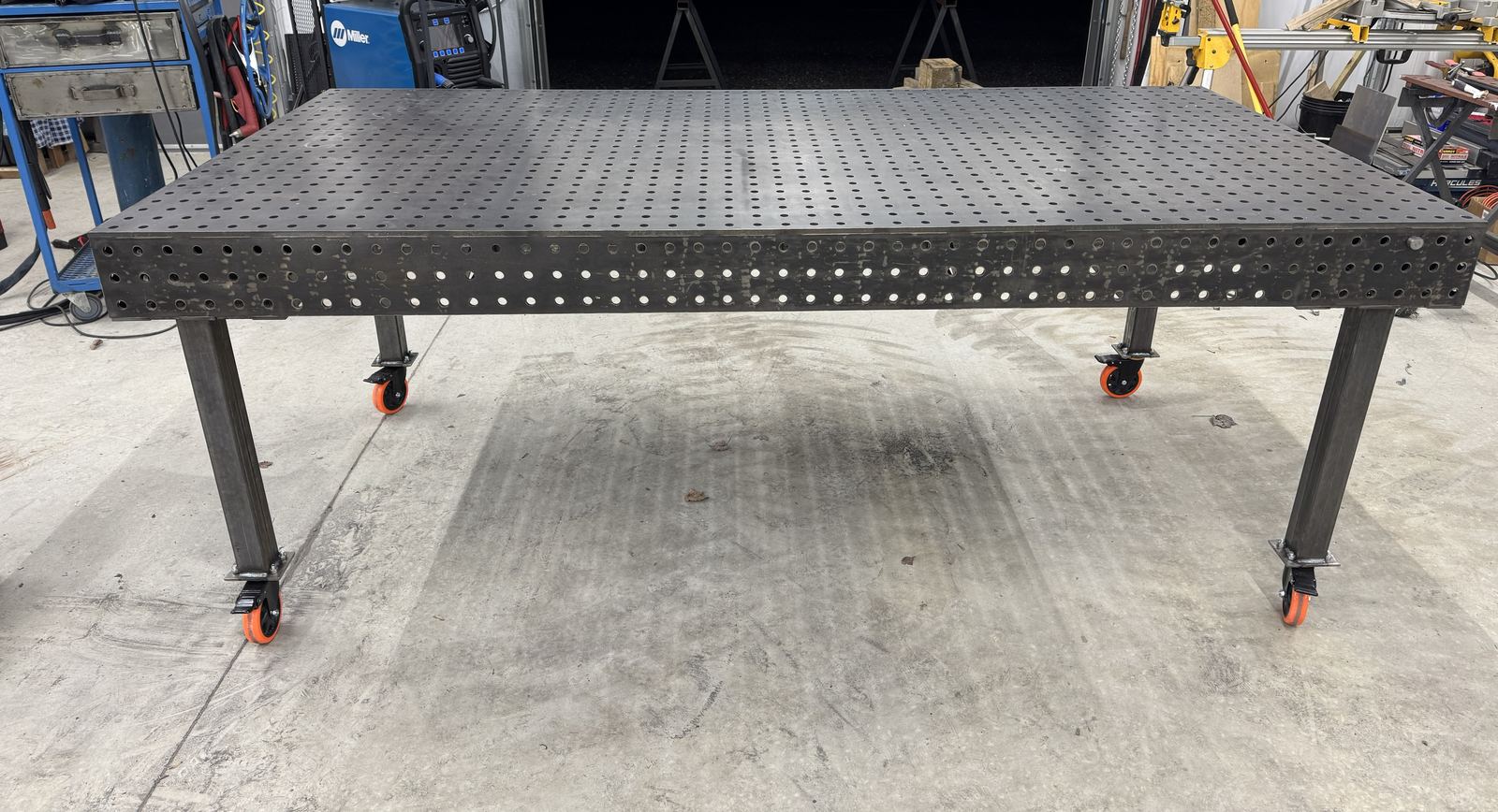 Finished 4 by 8 foot welding table with locking orange casters in a clean workshop